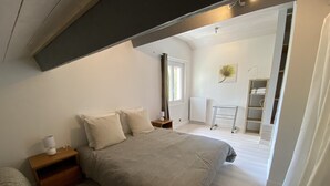 Ein Schlafzimmer mit einem großen Bett, einem Nachttisch mit Lampe, einem Heizkörper und einem kleinen Schreibtisch ebenfalls mit Lampe.