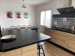 Een moderne keuken met een centraal eiland, zwarte aanstootplaten, houten kastjes en een betegelde achterwand.