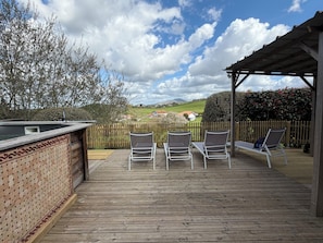 Een houten terras met lounge stoelen, een jacuzzi en uitzicht op het buitengebied.