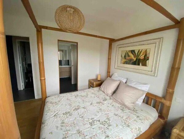 Een slaapkamer met een bloemenbedekker, houten hoofdbord en een schilderij aan de muur.
