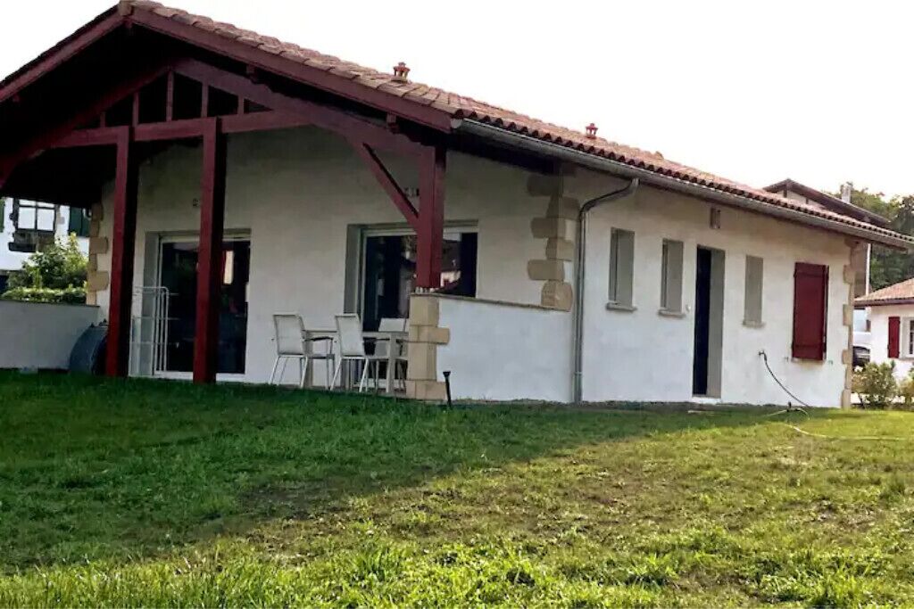 A single-story house with a red-tiled roof, a covered porch with chairs, and a small garden area.