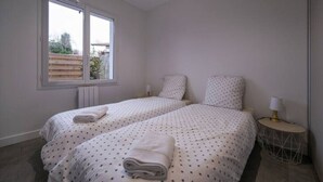 Una camera da letto con due letti, una finestra, un termosifone e un comodino con una lampada.