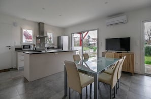 A modern kitchen with a dining area, a TV, and an air conditioning unit.