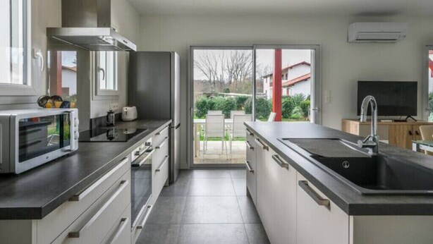 Una cucina moderna con un'isola grande, elettrodomestici integrati e una porta scorrevole in vetro che conduce a un patio.