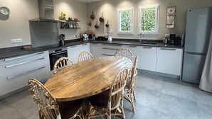 Una cocina moderna con una isla central, armarios blancos y una zona de comedor con sillas de mimbre.