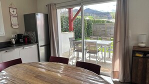 Una cocina equipada con refrigerador, cafetera y hervidor. Hay una mesa de comedor con sillas y vistas al exterior a través de una puerta corrediza de vidrio.