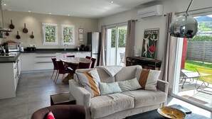 Una cocina moderna con armarios blancos, una zona de comedor con sillas rojas, un sofá gris con cojines estampados y una mesa de centro negra.