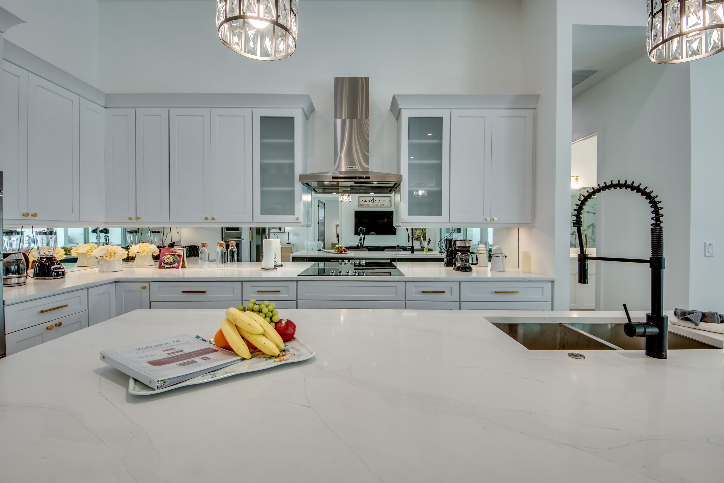 A modern kitchen with white cabinetry, a central island with fruits, and stainless steel appliances.