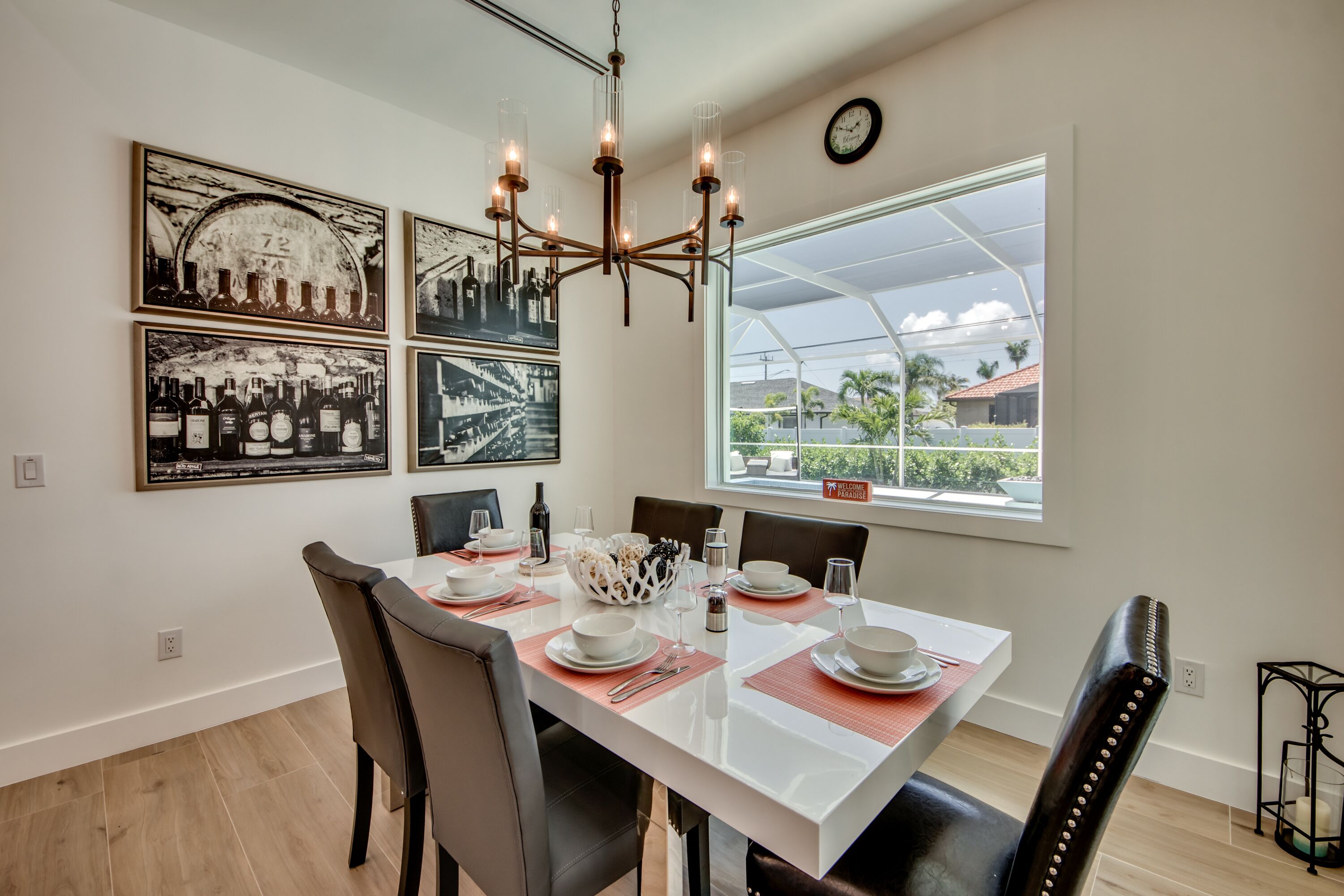 Un coin repas avec une table blanche dressée pour quatre personnes, entourée de chaises, d’un lustre et de tableaux encadrés accrochés au mur.