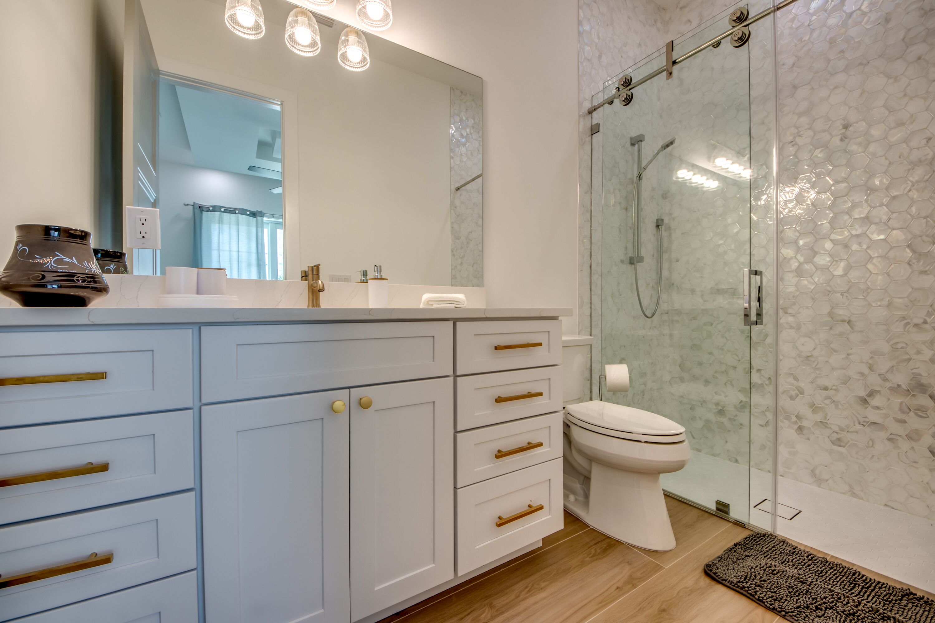 A modern bathroom with a glass shower enclosure, a white toilet, and a vanity with multiple drawers and a mirror.