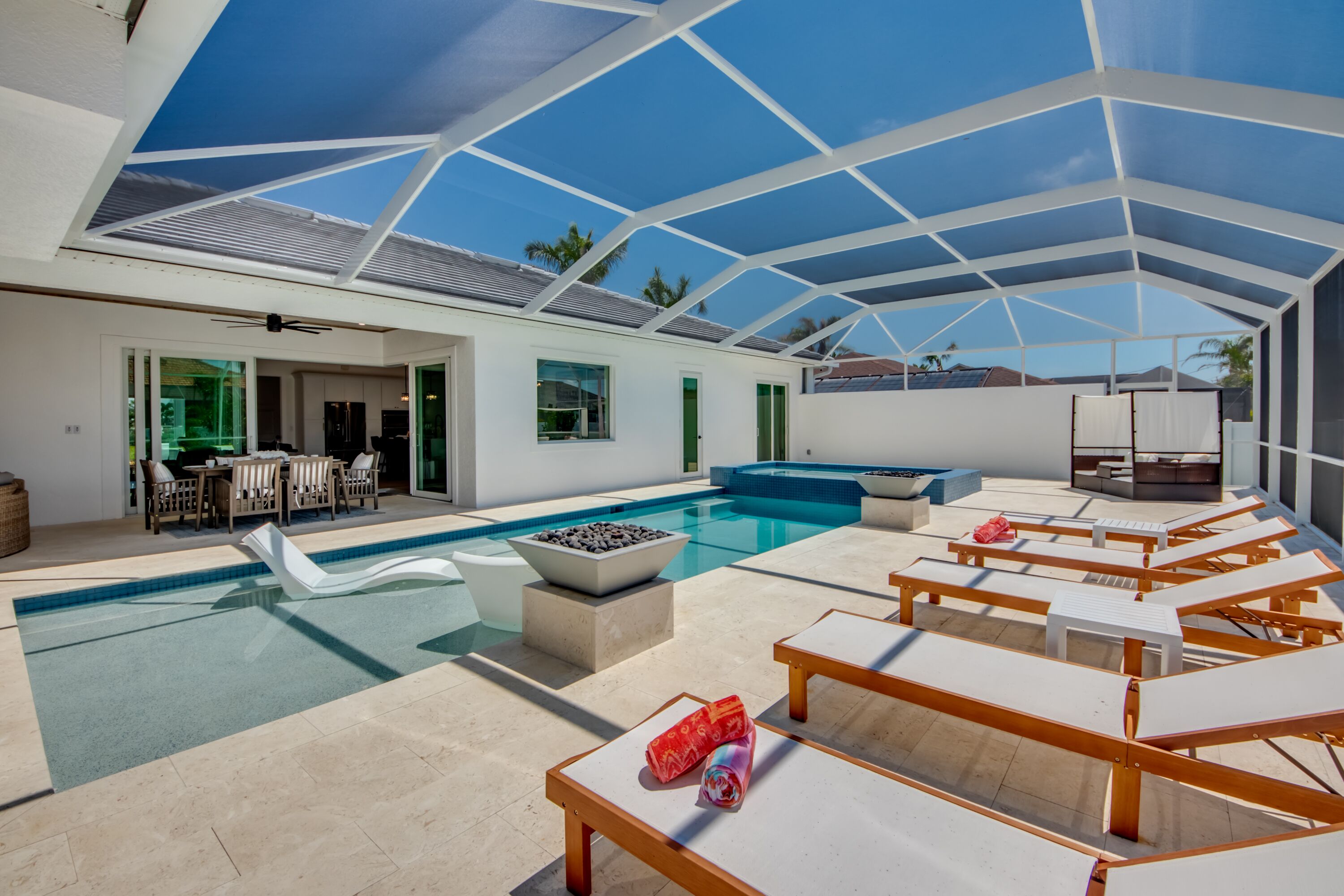 Ein moderner Poolbereich im Freien mit Liegestühlen, Essbereich und einer überdachten Terrasse.