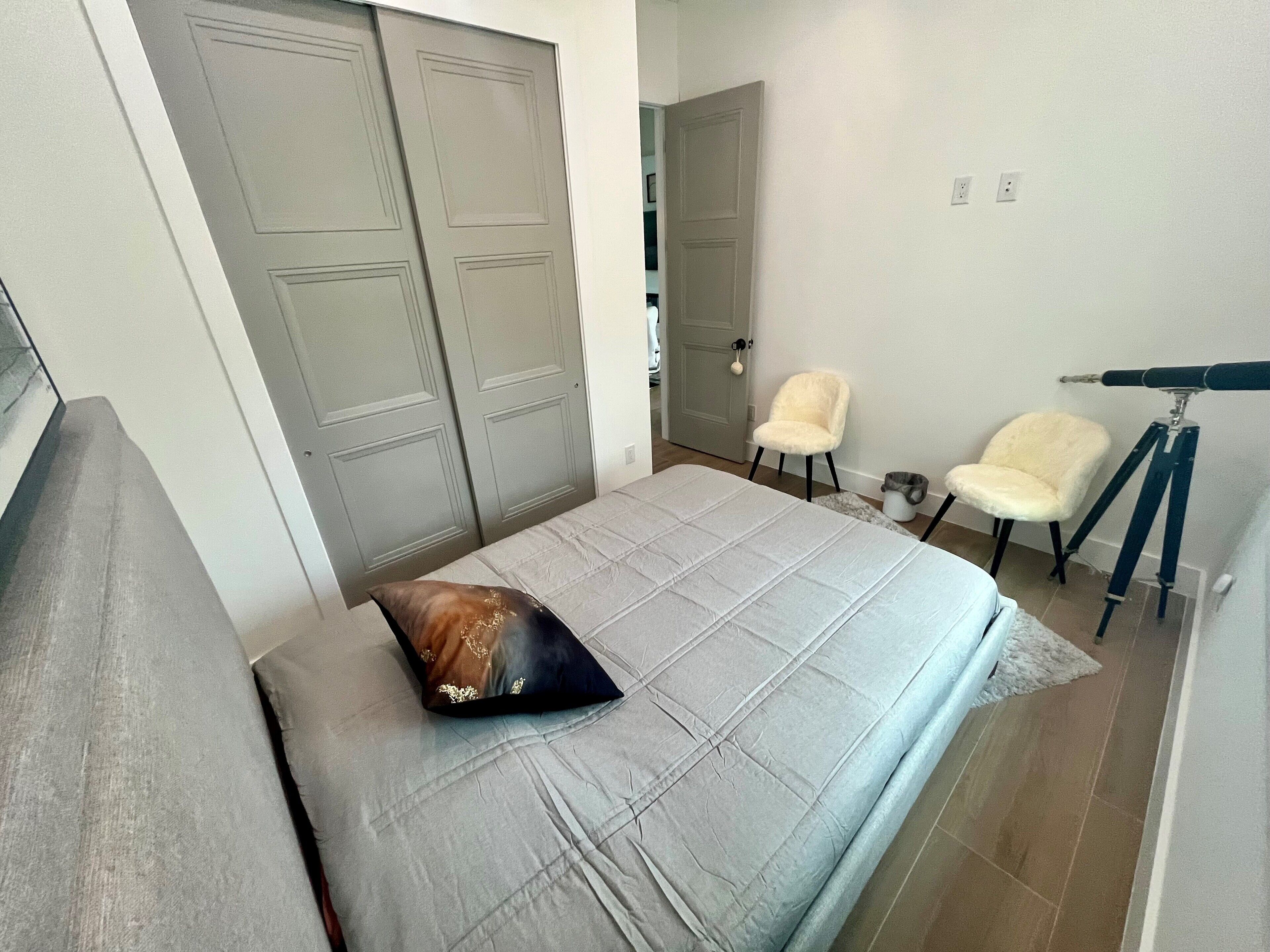Een slaapkamer met een bed, een kussen, twee stoelen, een telescoop en een deur.