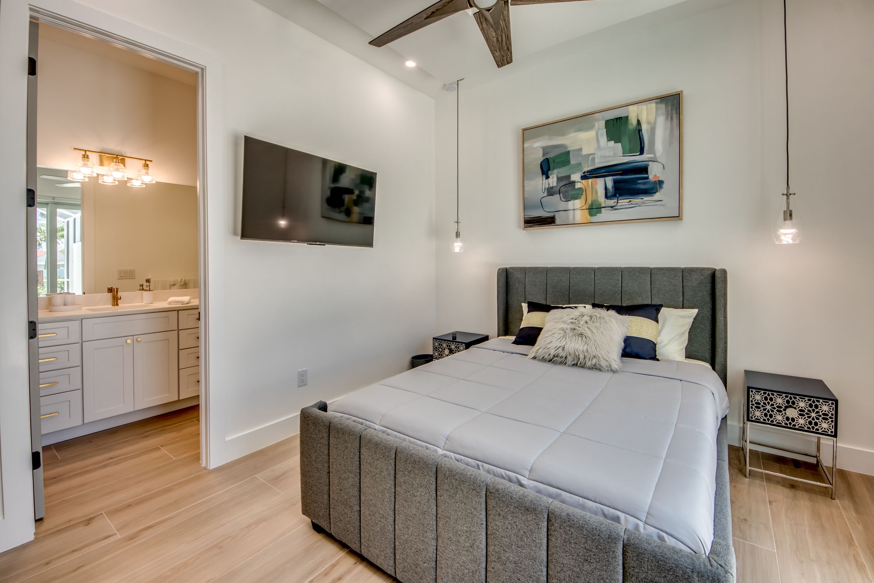 A modern bedroom with a large bed, a ceiling fan, a mounted TV, and a painting on the wall.