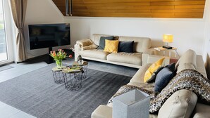 A modern living room with a sofa, a coffee table, a TV, and a lamp. - Charming Holiday House (Mastershausen)
