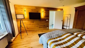 A bedroom with a wooden floor, a bed with striped bedding, a standing lamp, a flat-screen TV mounted on the wall, and a door leading to another room. - Charming Holiday House (Mastershausen)