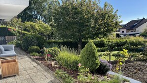 A garden with a patio area, a wooden bench, and various plants. - Charming Holiday House (Mastershausen)