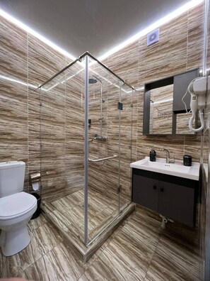 Un baño moderno con ducha envuelta en vidrio, inodoro blanco y lavamanos con espejo.