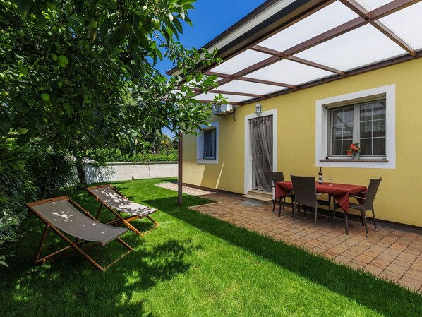 Relax in the serene patio area with a lawn, table, chairs, and sun loungers under a shaded pergola.