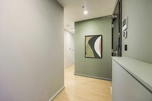 Un couloir au design moderne, avec un mur de couleur claire, un plancher en bois et une œuvre d’art abstraite encadrée.