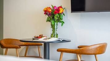 A modern room with a round table, two leather chairs, a vase of flowers, and a flat-screen TV mounted on the wall.