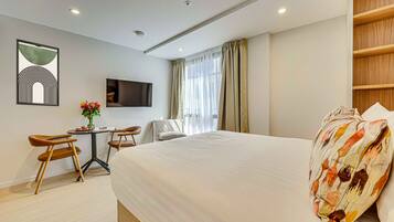 A hotel room with a large bed, a desk with two chairs, a TV mounted on the wall, and a window with curtains.