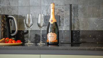 A bottle of champagne, two glasses, and a plate of strawberries on a kitchen counter.