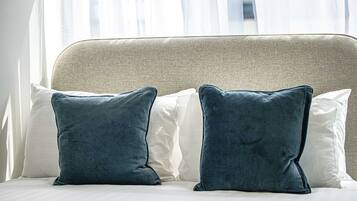 Cama com duas almofadas, cabeceira e janela com cortinas leves.