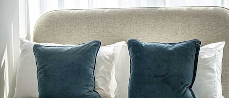 A bed with two pillows, a headboard, and a window with sheer curtains.