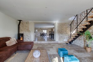 A spacious living area with a stone wall, a brown leather sofa, a wooden coffee table, and a staircase with a metal railing. - Les Bellangers 1 - Piscine et Jacuzzi (Artigues)