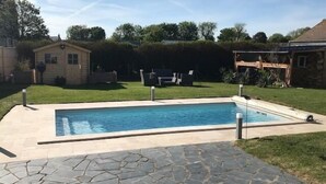 Ein rechteckiger Swimmingpool mit einer Steinterrasse davor, umgeben von einem Rasen und einer Holzterrasse.