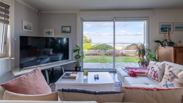 Ein Wohnzimmer mit Fernseher, Sofa, Couchtisch und Blick ins Freie.