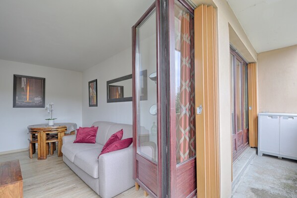 A living room with a sofa, a wooden table, and a glass door leading to a balcony. - Swingcat - Charmant appt pour 2 (Athis Mons)