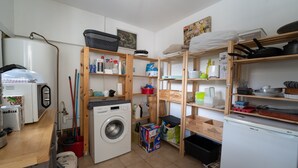 Cocina compacta con lavadora, refrigerador y estanterías de madera con diversos utensilios de cocina.