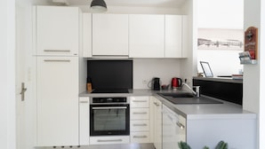 Una cocina moderna con armarios blancos, un horno negro, un lavamanos y una lámpara colgante.