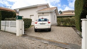 Un coche blanco aparcado en un camino de grava frente a una casa blanca con tejado de tejas.