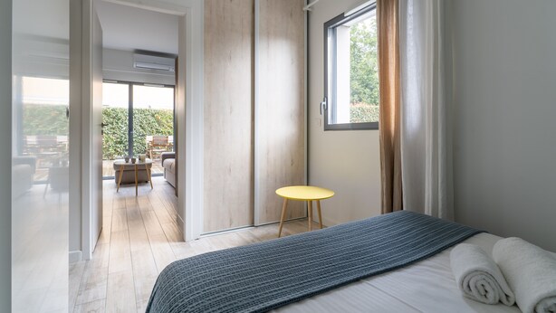 Un dormitorio con cama, ventana, puerta corredera y vistas a un espacio exterior.