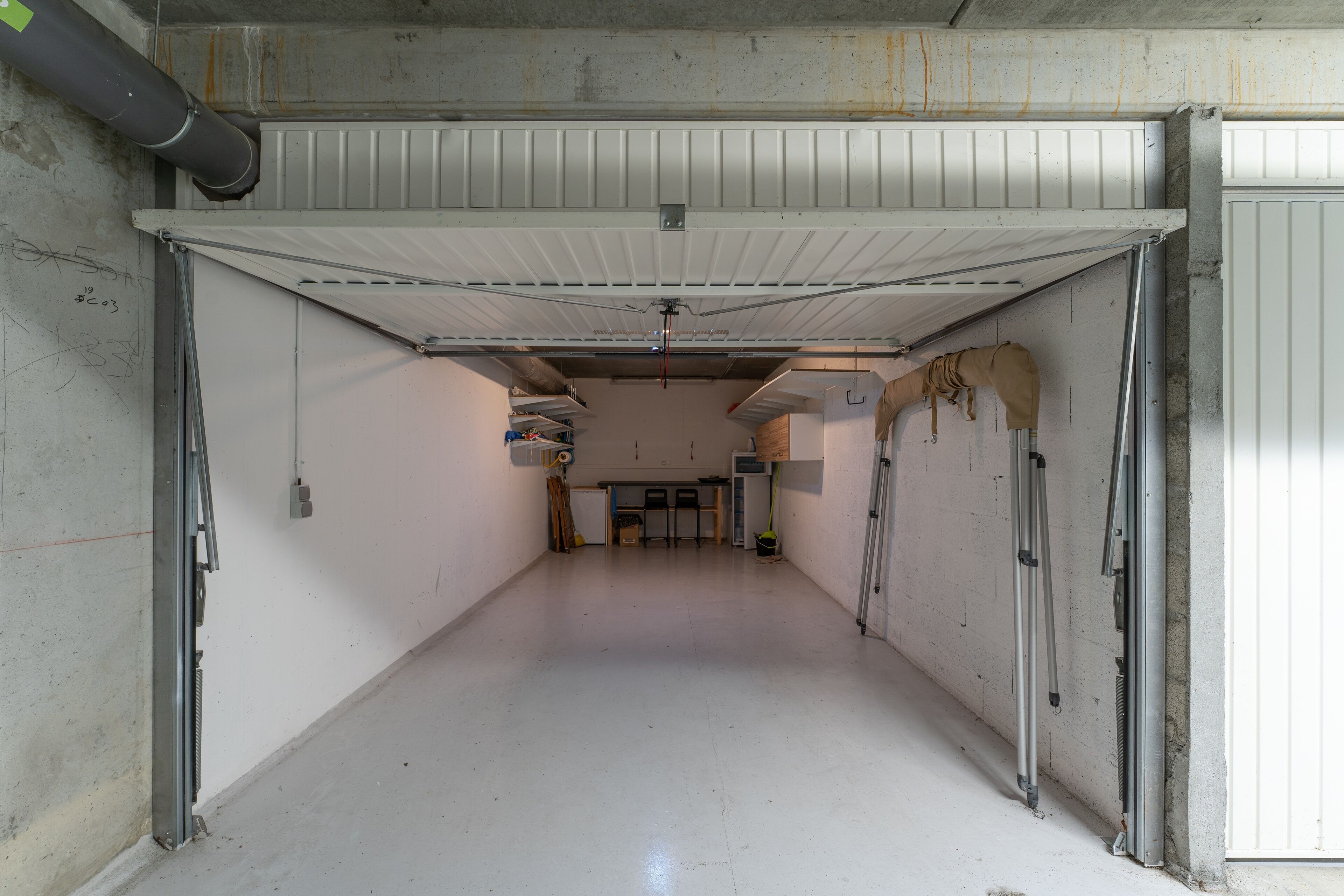 Un pasillo limpio y vacío con techo blanco, paredes de concreto y una puerta de garaje cerrada.