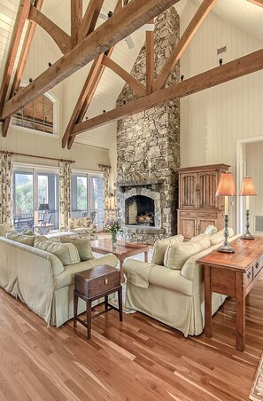 A spacious living room with wooden beams, a stone fireplace, and a large sofa set.