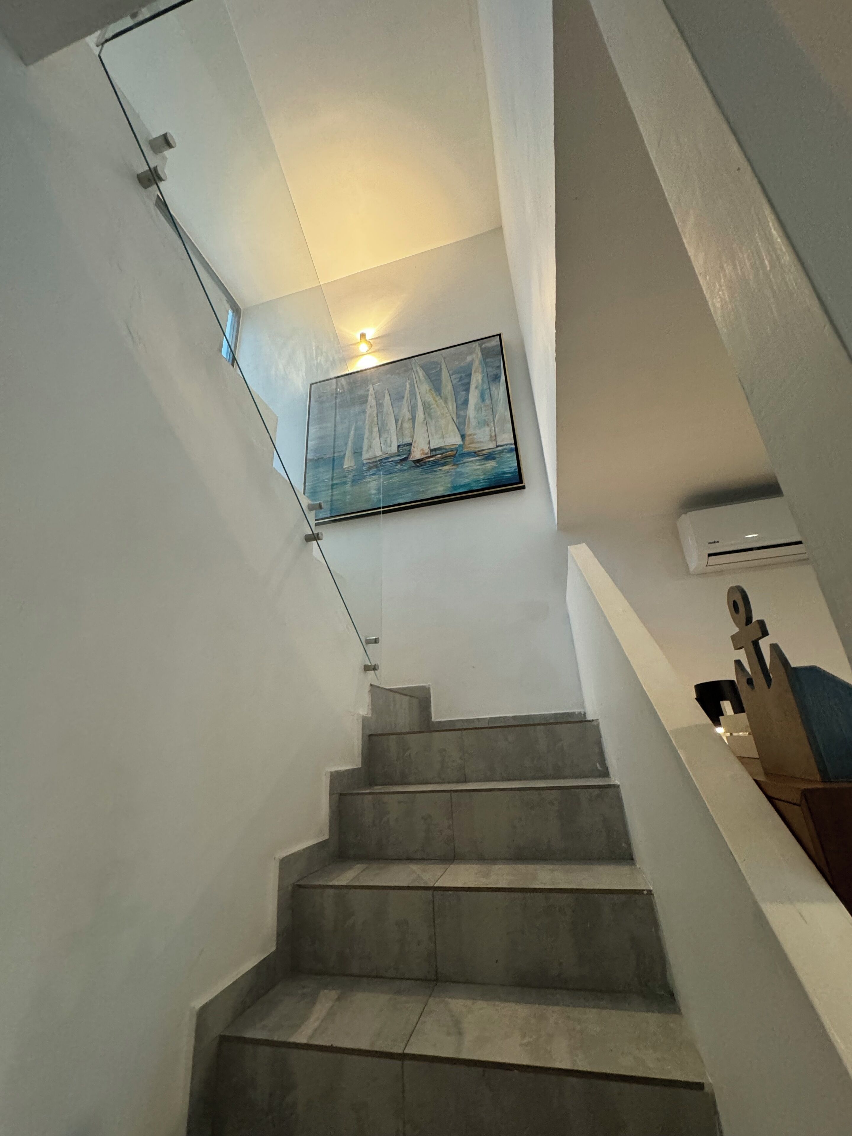 Una escalera con barandilla de vidrio y un cuadro con barcos a vela en la pared.