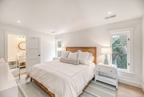 A bedroom with a large bed, bedside tables, a nightstand, a dresser, and a window with a view of greenery.