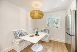 A modern kitchen with a white table, bench seating, a large window, and a stainless steel refrigerator.