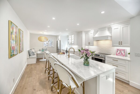 A modern kitchen with white cabinetry, a central island with bar stools, a stainless steel refrigerator, and a built-in oven.