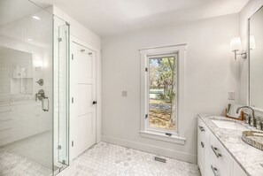 A modern bathroom with a glass-enclosed shower, a large window, and a marble sink.