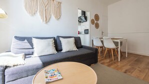Un salon moderne avec un canapé gris, des coussins blancs, une table basse ronde en bois et une petite table blanche avec des chaises.