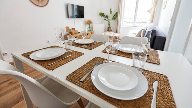 Une table à manger dressée avec de l’argenterie blanche, des verres transparents et des couverts, le tout entouré de sets de table en fibres tressées.
