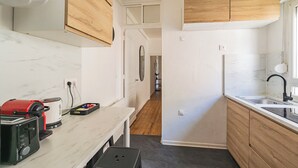 Una cocina compacta con armarios de madera, encimera de mármol, refrigerador integrado y un lavamanos.