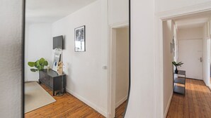 Un pasillo con piso de madera, un mueble oscuro con una planta, un cuadro enmarcado y una puerta que da a otra habitación.