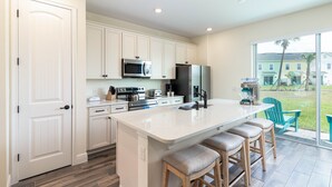 A modern kitchen with white cabinetry, stainless steel appliances, and a large island with bar stools. - Margaritaville Townhome Retreat (Kissimmee)