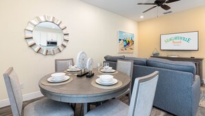 A dining area with a round table set for four, a gray sofa, and a ceiling fan. - Margaritaville Townhome Retreat (Kissimmee)