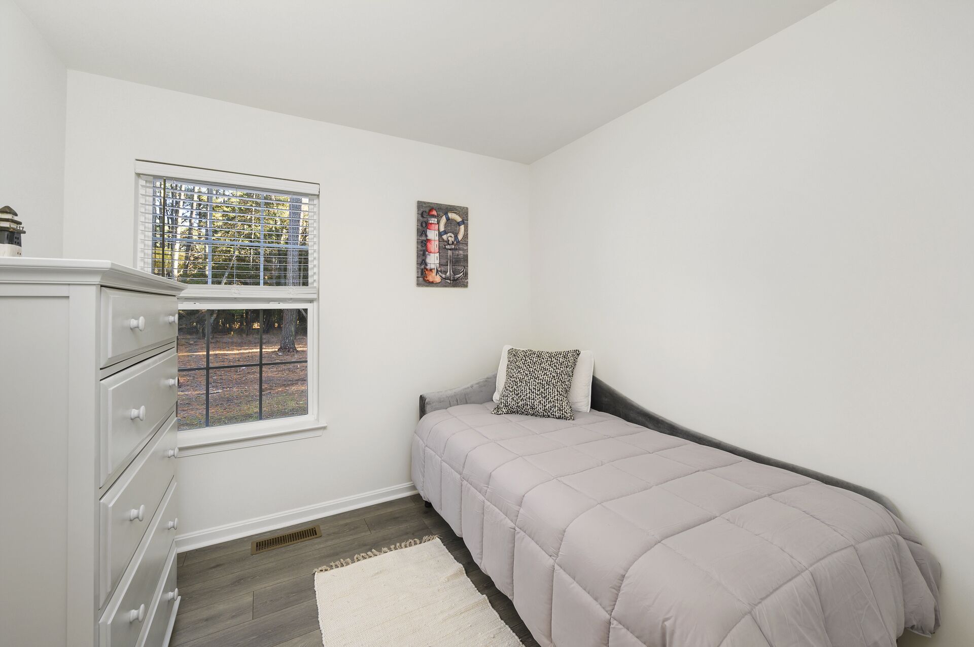 A bedroom with a bed, a dresser, a window, and a painting.